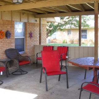 A cozy covered patio with red chairs and a round table, set against a brick wall backdrop.