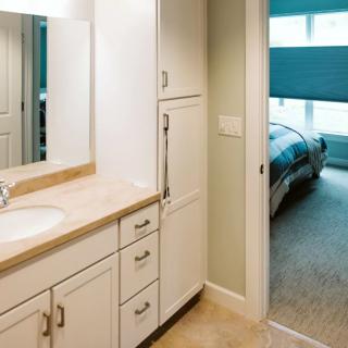 A modern bathroom with a sink and vanity, showing a view into the adjacent bedroom.