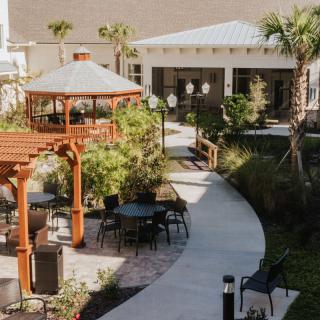 A tranquil outdoor garden featuring a gazebo, pathway, and seating areas surrounded by lush greenery.