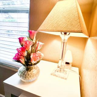 A cozy setup with a lamp and pink flowers in a vase on a table by the window.