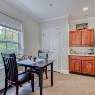 A cozy dining area featuring a dark wooden table with chairs, a window letting in natural light, and wooden cabinets.