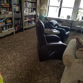 A cozy living room with bookshelves, armchairs, and a large window.