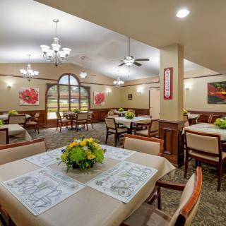 A well-appointed dining room featuring multiple tables with decorative centerpieces, comfortable chairs, and elegant lighting fixtures.