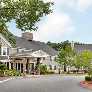 A scenic view of a large residential building with a landscaped driveway and surrounding greenery.