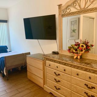 A cozy bedroom featuring a dresser with a mirror, a mounted television, and a vibrant flower arrangement.