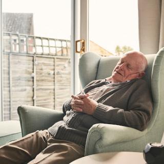 An elderly man peacefully resting in a comfortable chair by the window.