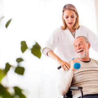 A caregiver assists an elderly man with physical exercises using a dumbbell.