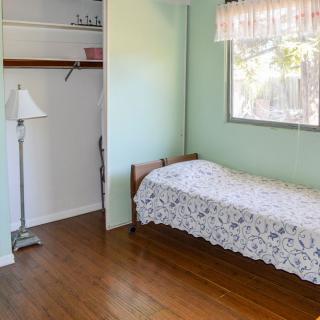 A simple bedroom with a single bed, wooden flooring, and a small closet.