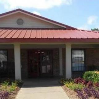 A small building with a red metal roof, front entrance, and garden.