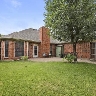 A spacious backyard with a brick house, well-maintained lawn, and a patio area.
