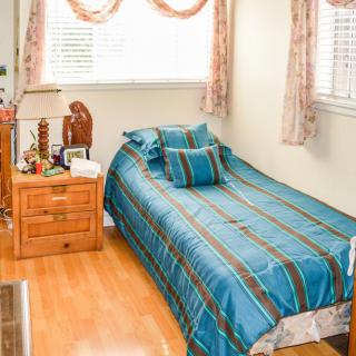 A cozy bedroom with a single bed featuring striped bedding, a wooden nightstand with a lamp, and window blinds letting in natural light.