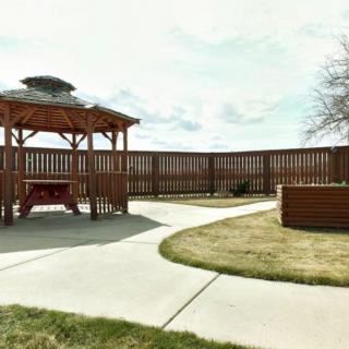 A peaceful outdoor area featuring a wooden gazebo, paved walkway, and surrounding fence under a cloudy sky.