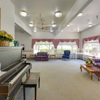 A spacious living room featuring a piano and comfortable seating, illuminated by natural light from large windows.
