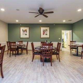 A dining room with several tables and chairs, featuring wood flooring, wall art, and a ceiling fan.