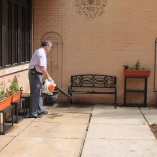 A person using a leaf blower on a patio area with planters and a bench.