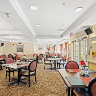 A spacious and elegantly decorated dining room with multiple tables and chairs, featuring large windows and ambient lighting.