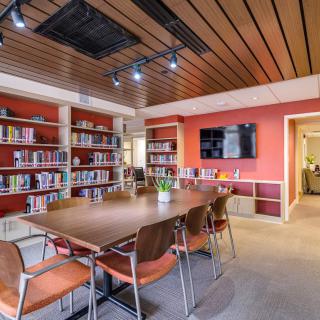 A modern conference room with a large meeting table surrounded by chairs, bookshelves lining the walls, and a television mounted on the wall.