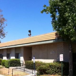 A one-story office building with a tree and parking area under a clear blue sky.