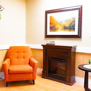 A cozy living room corner featuring an orange armchair, a stylish fireplace, and decorative artwork on the wall.