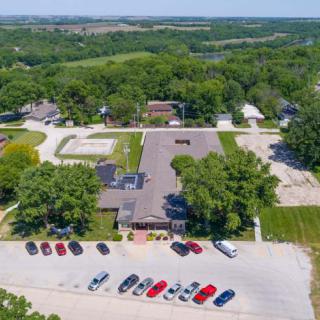 Aerial view of a building surrounded by trees with a parking lot and several cars in front.