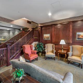 A cozy living room with comfortable armchairs and elegant wood paneling, featuring a staircase in the background.