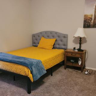 A cozy bedroom with a single bed featuring yellow bedding and a blue blanket, accompanied by a wooden nightstand and lamp.