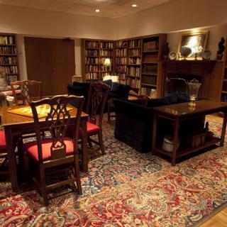 A cozy library room with bookshelves, a table with chairs, and a patterned carpet.