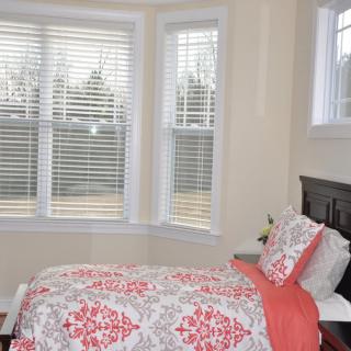 A cozy bedroom with a single bed and large windows adorned with blinds.