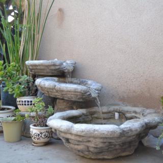 A tiered stone fountain surrounded by potted plants in an outdoor garden setting.