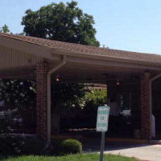 A driveway entrance with a canopy and parking sign, surrounded by trees.