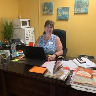 A woman sitting at a desk in an office with a laptop and various books and papers.