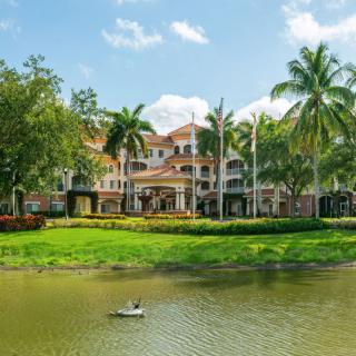A scenic view of a resort building surrounded by palm trees and a tranquil lake.