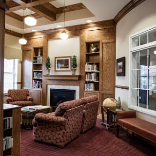 A cozy library interior featuring comfortable seating, a fireplace, and bookshelves filled with books.