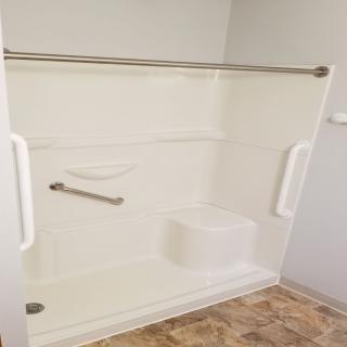 A bathroom with an accessible shower featuring grab bars and a bench.
