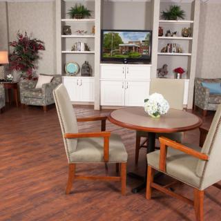 A cozy living room with a round table, upholstered chairs, and a television surrounded by bookshelves.