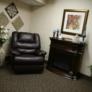 A cozy living room corner featuring a leather recliner, an electric fireplace, artwork on the wall, and decorative elements including a vase with flowers and candles.