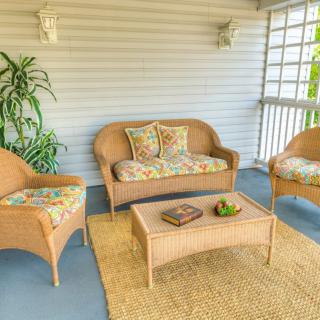 A cozy porch with wicker furniture, including a sofa and armchairs, decorated with colorful cushions and a rug.