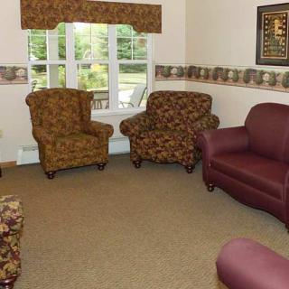A cozy living room with patterned armchairs, a leather sofa, and a large window providing natural light.