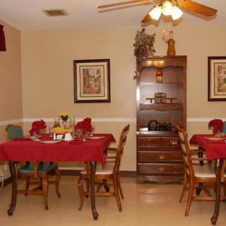 A cozy dining room with tables covered in red tablecloths, surrounded by wooden chairs and decorated with wall art and a cabinet.