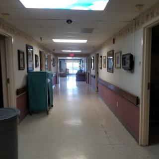 A well-lit hospital hallway featuring framed artwork on the walls and cleaning equipment positioned to the side.