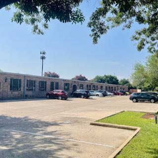A view of a parking lot with several cars in front of a row of buildings on a sunny day.