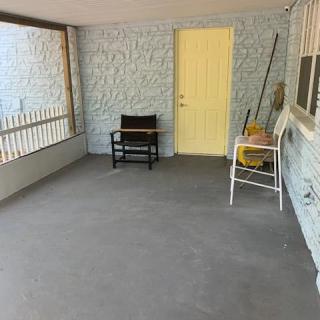 A simple porch with a chair, small table, and yellow door.