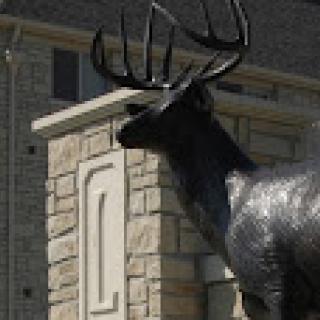 A striking statue of a deer with prominent antlers, standing near a stone structure.