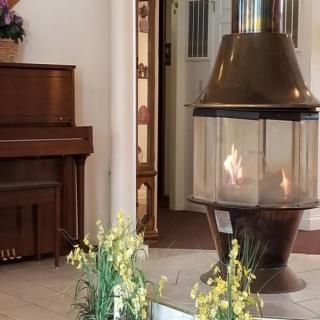 A cozy interior featuring a modern fireplace, a piano, and decorative floral arrangements.