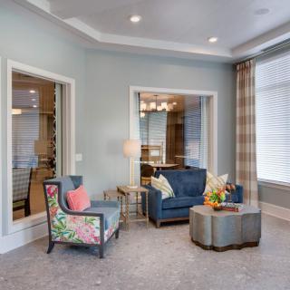 A cozy living room with armchairs, an ottoman, and a floor lamp, featuring large windows and elegant curtains.