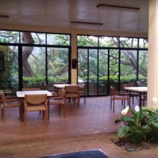 A dining area with large windows overlooking lush greenery, featuring tables and chairs arranged neatly.