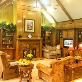A cozy living room with traditional wood paneling and a vaulted ceiling, featuring comfortable seating around a fireplace and television.