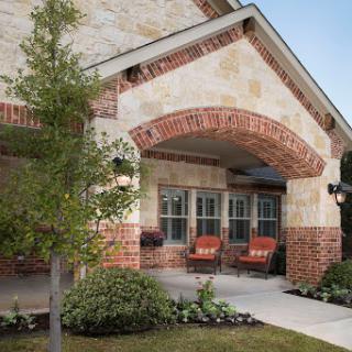 A beautifully designed house featuring a brick and stone exterior, complemented by a welcoming porch and garden.