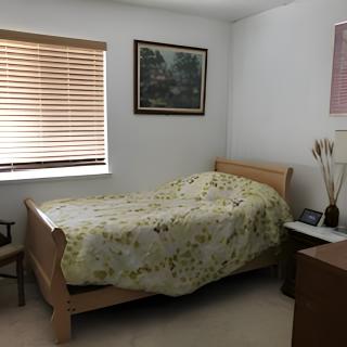 A cozy bedroom with a single bed featuring a floral bedspread, a window with blinds, and a painting on the wall.