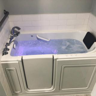 A walk-in bathtub filled with water, featuring a safety handle and tile backsplash.